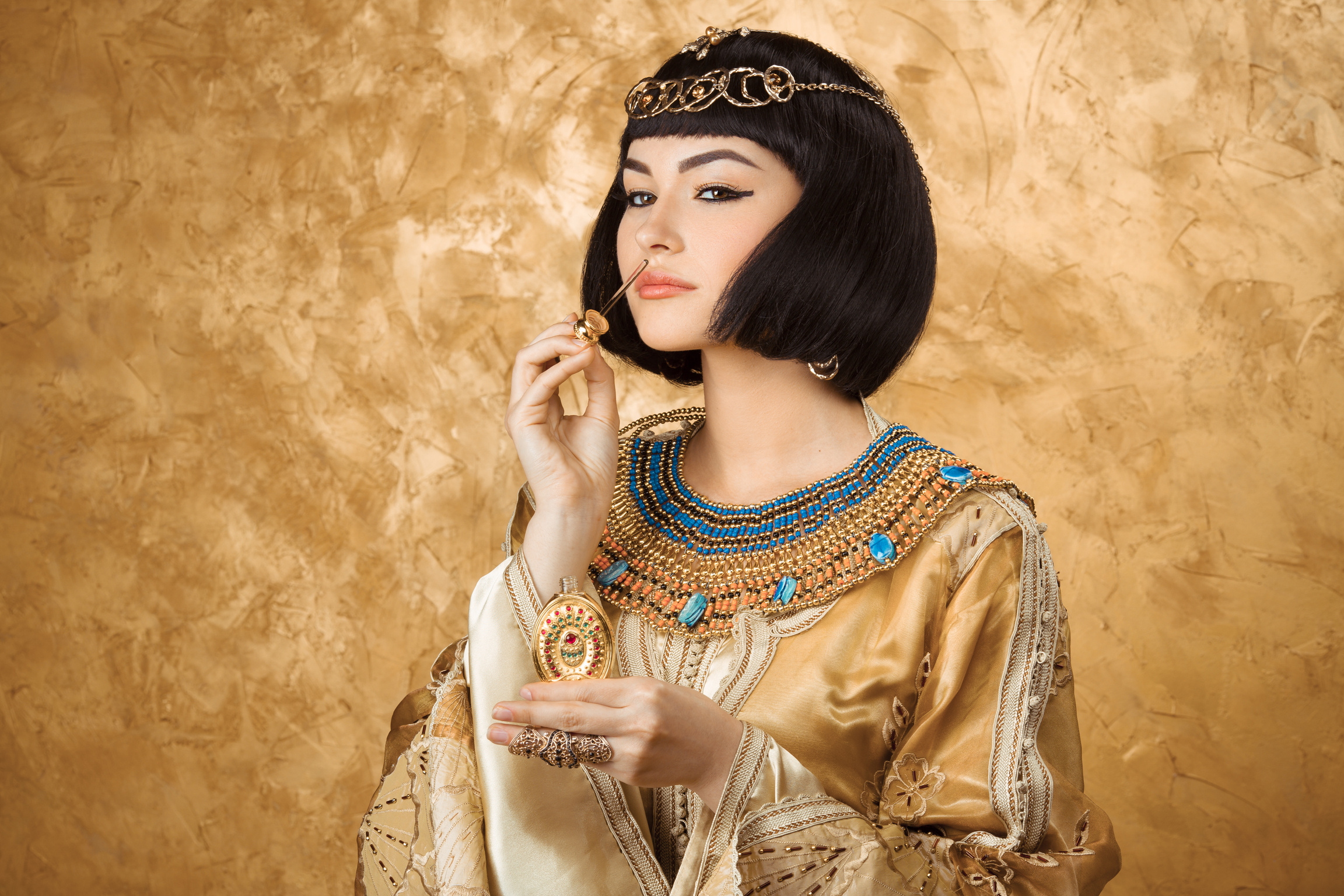 Beautiful Egyptian woman like Cleopatra with perfume bottle on golden